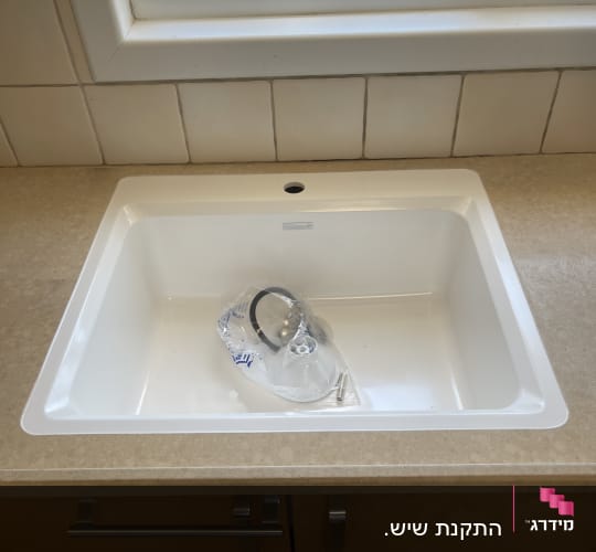 כיור מטבח עם חלון ברקע וחלקים באריזה